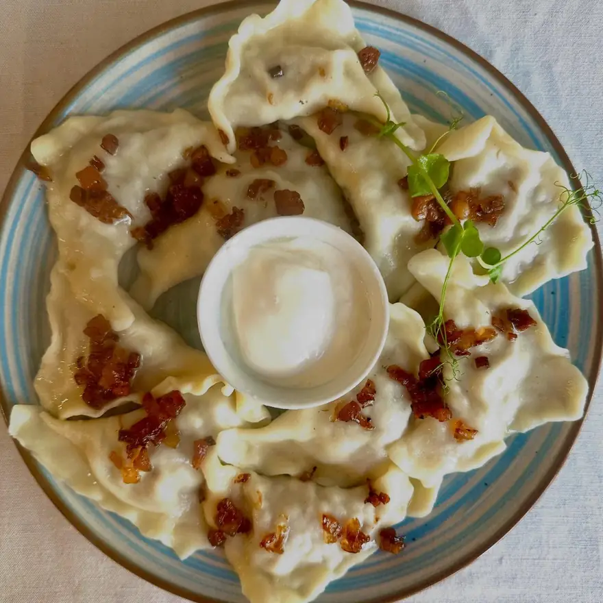 Talerz pierogów ze skwarkami i miseczką śmietany, widok z góry